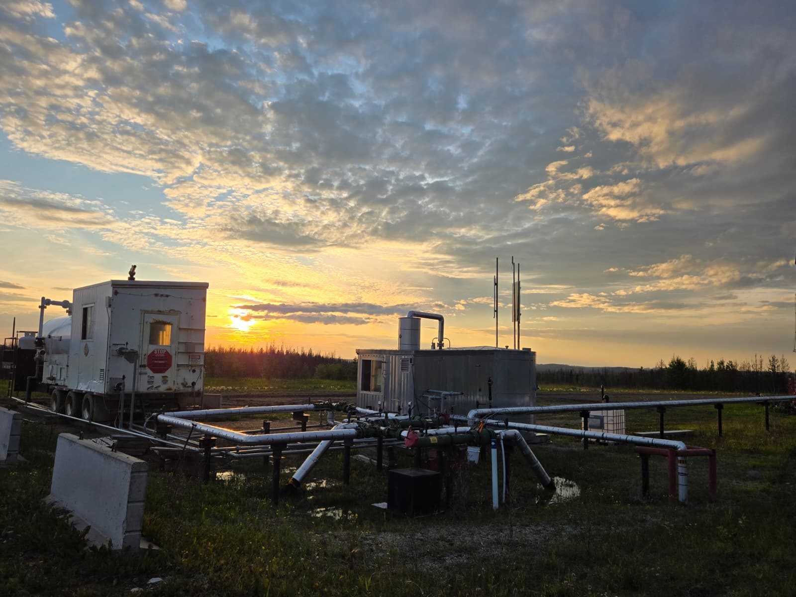 Wellsite at sunset with natural gas generation and containerised mining infrastructure alongside producing oil and gas equipment.