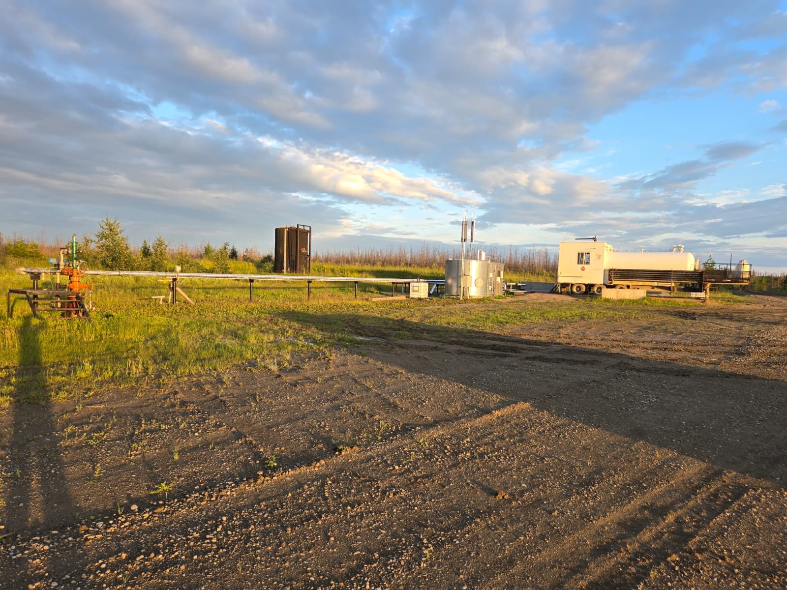 Wellsite at dusk with pipework and equipment.